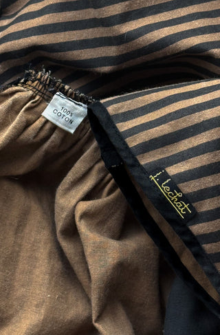 Close-up of striped brown and black dress with a white '100% COTTON' label, and a small gold embroidered 'J Lechat' logo.