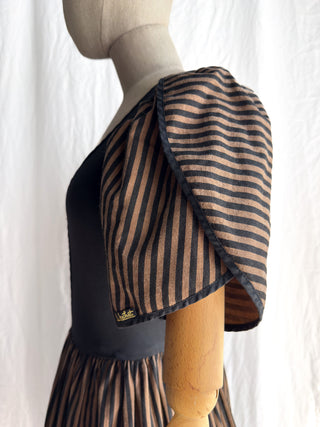 A close-up side view of a dress displayed on a mannequin against a white curtain background. The dress has black body with striped puffy petal sleeves