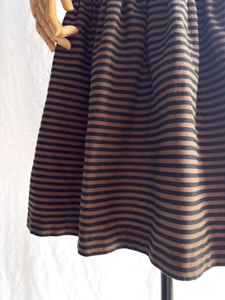 A close-up of a skirt on a 1970s vintage French striped dress on a mannequin with a wooden hand visible at the top left against a white fabric backdrop.