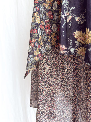 A close-up of a sheer floral fabric garment or drape, showing layered floral prints in dark purple, black, beige, and muted red tones against a white background.